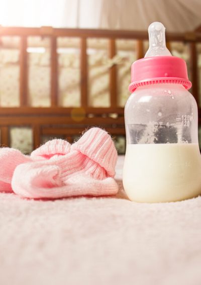 Pink baby booties and bottle of formula with crib