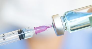 doctor's hand holds a syringe and a blue vaccine bottle at the hospital. Health and medical concepts.